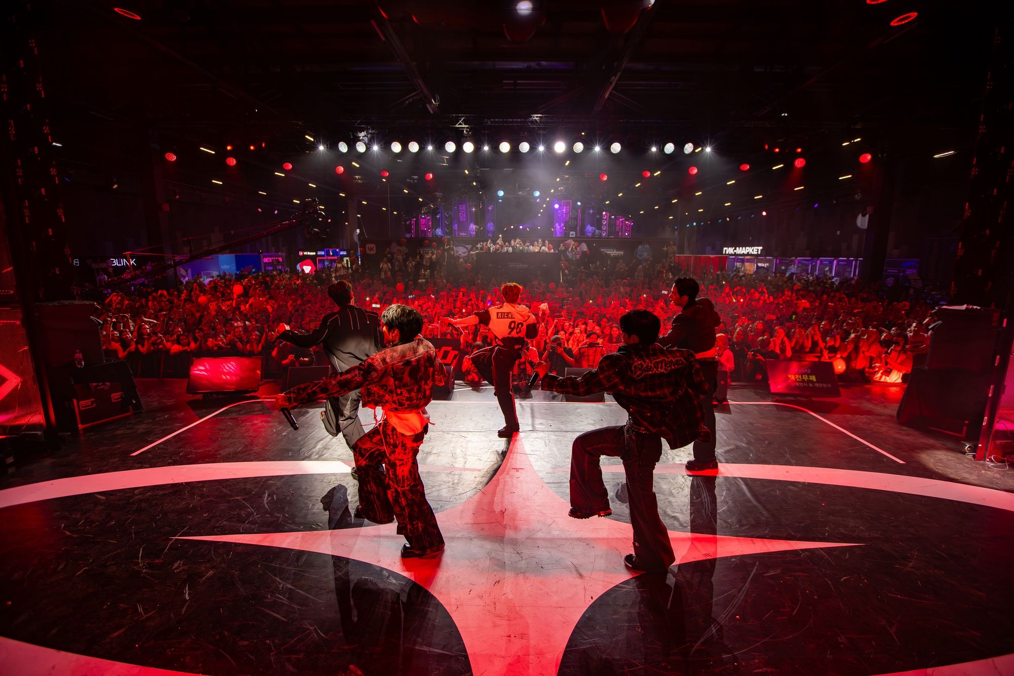 TAPE Agency artists performing on a red-lit arena stage in front of a full crowd